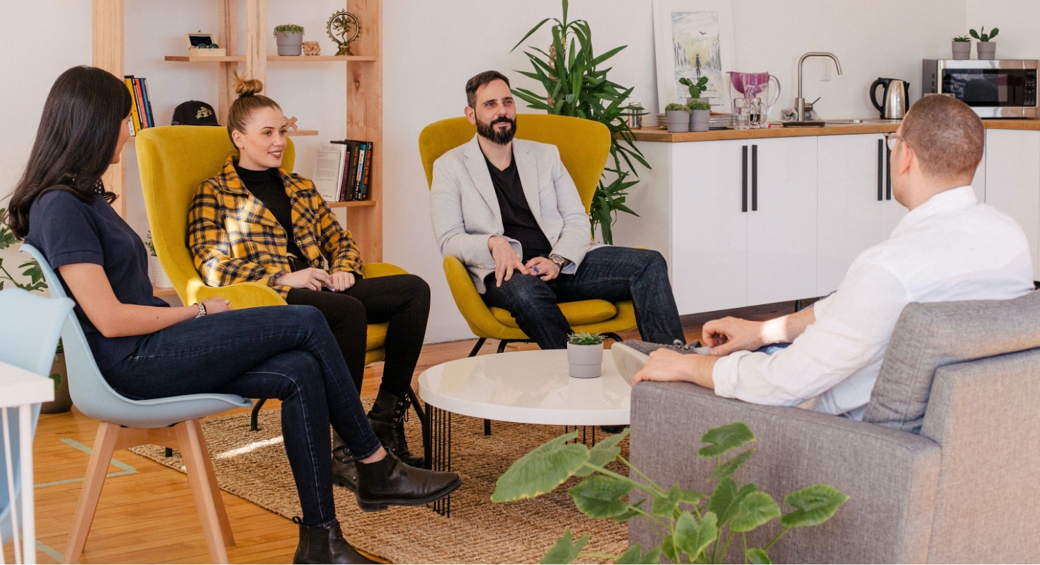 Four people sat in comfy chairs around a small coffee table in an office environment talking